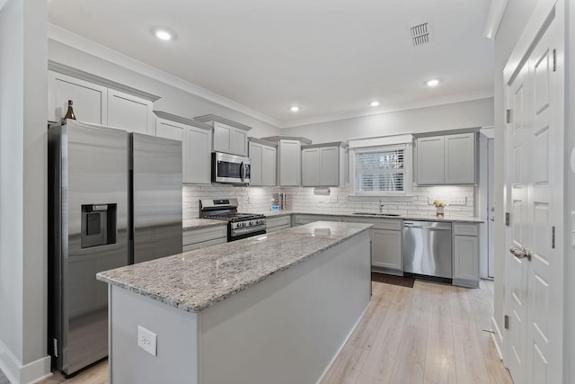 kitchen featuring sink, light hardwood / wood-style flooring, appliances with stainless steel finishes, a kitchen island, and light stone counters