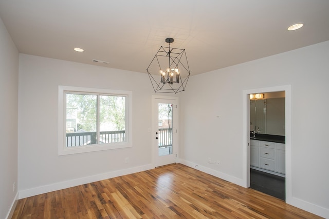 spare room with hardwood / wood-style floors and an inviting chandelier