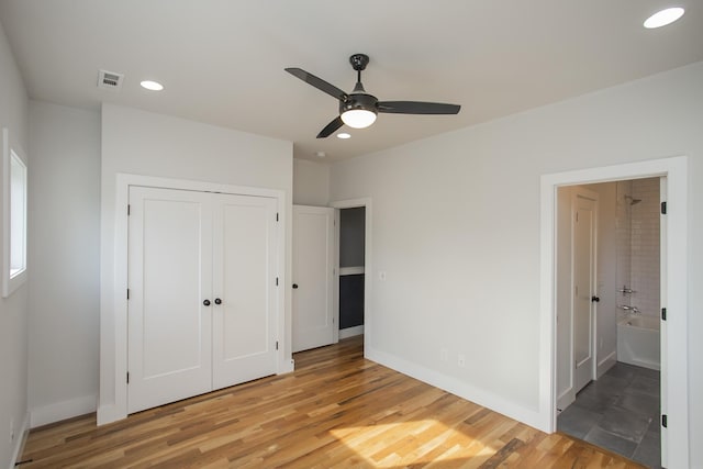 unfurnished bedroom with ceiling fan, a closet, wood-type flooring, and ensuite bath