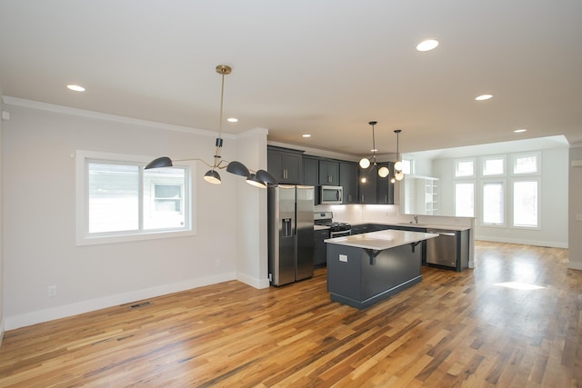 kitchen featuring hanging light fixtures, a kitchen breakfast bar, appliances with stainless steel finishes, a kitchen island, and ornamental molding