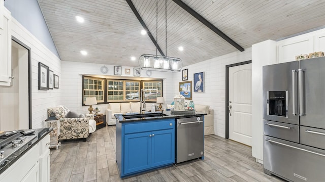 kitchen featuring stainless steel appliances, wooden walls, sink, blue cabinetry, and white cabinets