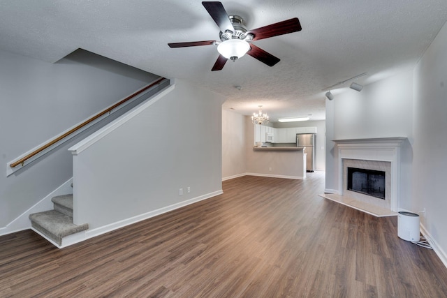 unfurnished living room featuring dark wood-type flooring, ceiling fan with notable chandelier, rail lighting, a premium fireplace, and a textured ceiling