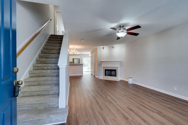 unfurnished living room with a textured ceiling, ceiling fan with notable chandelier, and hardwood / wood-style flooring