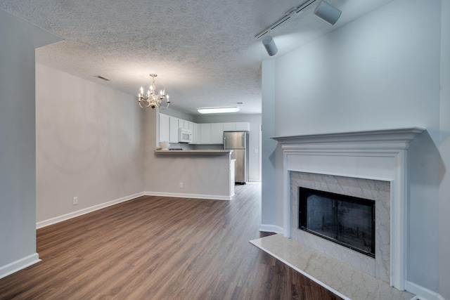 unfurnished living room featuring an inviting chandelier, rail lighting, hardwood / wood-style flooring, a textured ceiling, and a fireplace