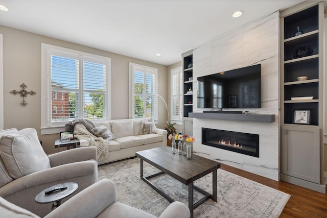 living room featuring a tile fireplace, built in features, and wood-type flooring