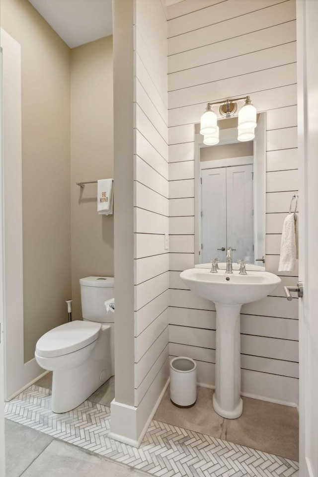 bathroom with toilet, tile patterned floors, and wooden walls