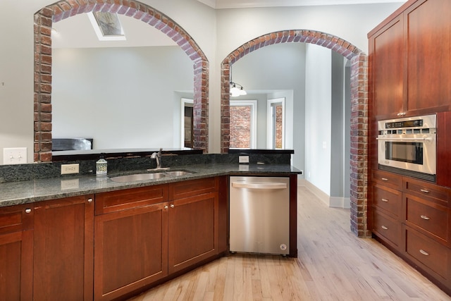 kitchen with light hardwood / wood-style flooring, dark stone countertops, sink, and stainless steel appliances