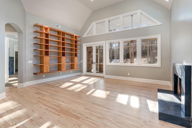 unfurnished living room with plenty of natural light, light wood-type flooring, high vaulted ceiling, and french doors