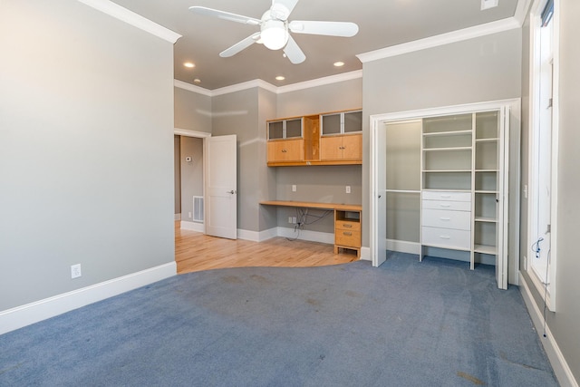 unfurnished bedroom with ceiling fan, built in desk, ornamental molding, and carpet floors