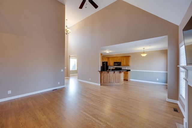 unfurnished living room featuring ceiling fan with notable chandelier, light wood-type flooring, and high vaulted ceiling