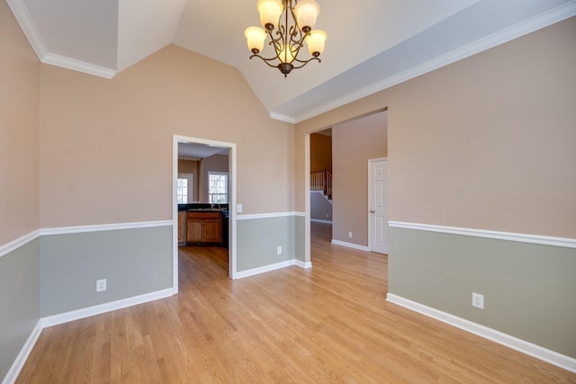 spare room featuring crown molding, light hardwood / wood-style flooring, lofted ceiling, and a notable chandelier