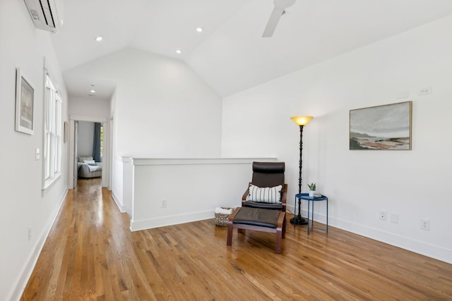 sitting room featuring light wood-type flooring, vaulted ceiling, a wall mounted AC, and ceiling fan