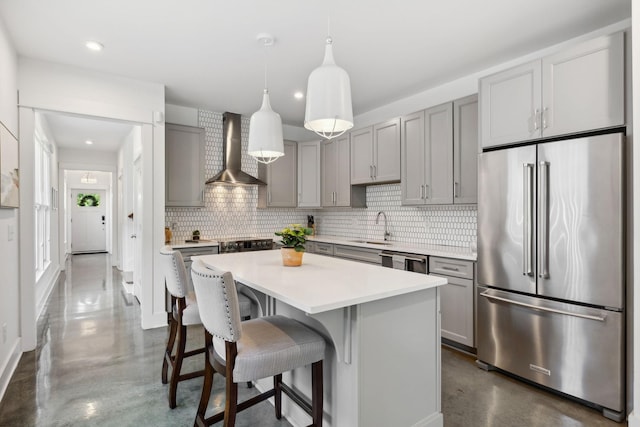 kitchen with sink, wall chimney exhaust hood, decorative light fixtures, high end fridge, and a kitchen island