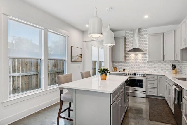 kitchen with a kitchen bar, appliances with stainless steel finishes, gray cabinetry, wall chimney range hood, and decorative light fixtures