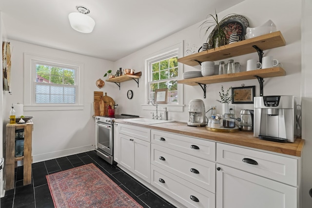 kitchen with wooden counters, sink, dark tile patterned flooring, white cabinetry, and stainless steel range with electric cooktop