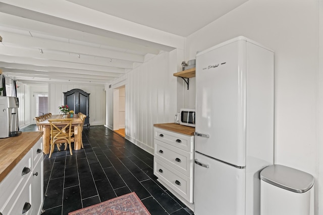 kitchen featuring butcher block counters, beamed ceiling, white cabinets, and white appliances