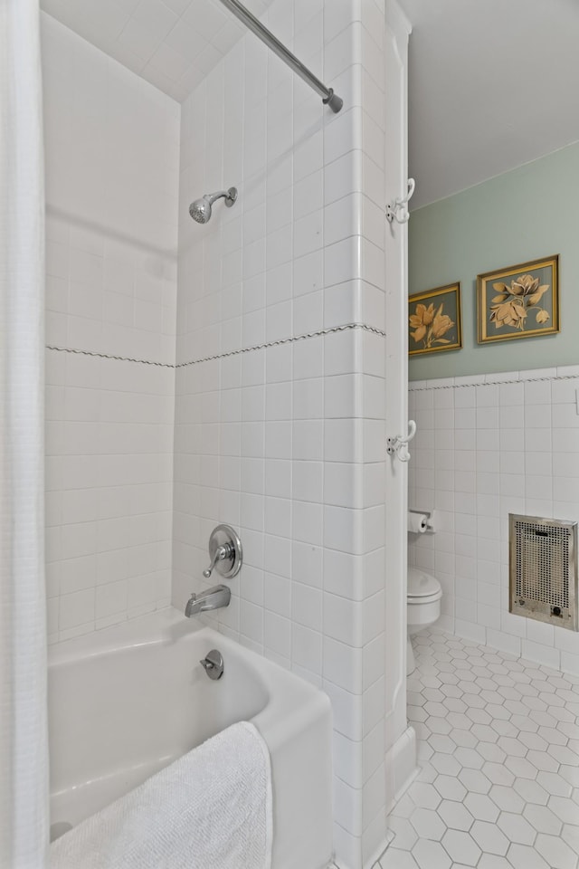 bathroom with tile patterned flooring, heating unit, tile walls, toilet, and shower / tub combo