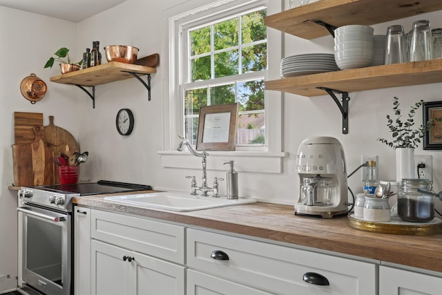 kitchen with butcher block counters, sink, white cabinets, and stainless steel range with electric stovetop