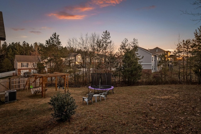 yard at dusk featuring a trampoline and central AC