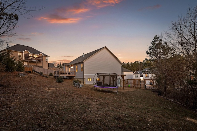 back house at dusk featuring a trampoline and a wooden deck