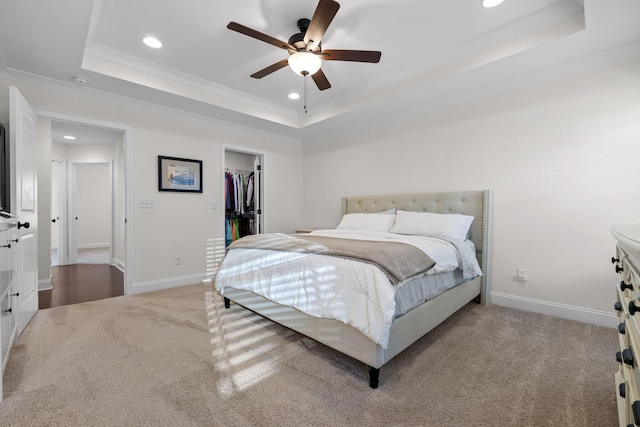 carpeted bedroom featuring ceiling fan, a raised ceiling, a walk in closet, and a closet