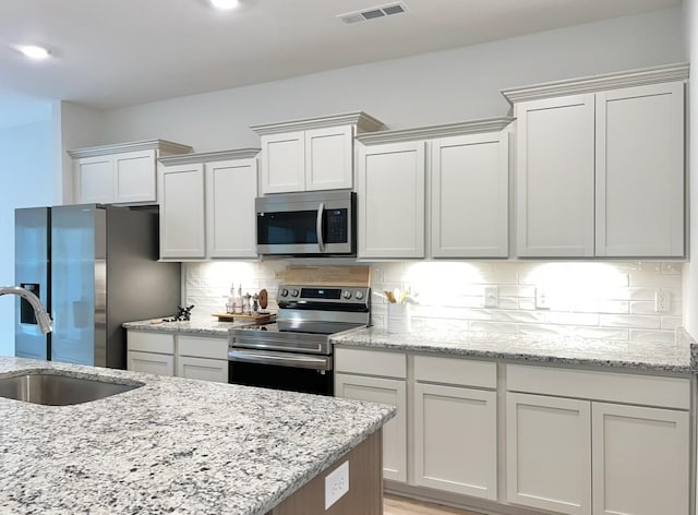 kitchen with light stone countertops, tasteful backsplash, stainless steel appliances, sink, and white cabinetry