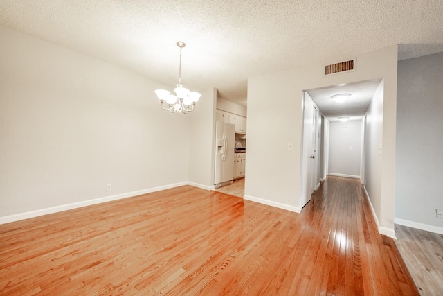 empty room featuring a textured ceiling, light wood-type flooring, and an inviting chandelier