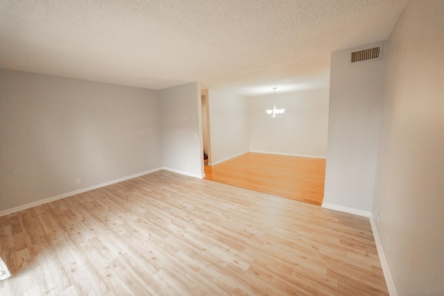 spare room featuring a notable chandelier, light hardwood / wood-style floors, and a textured ceiling