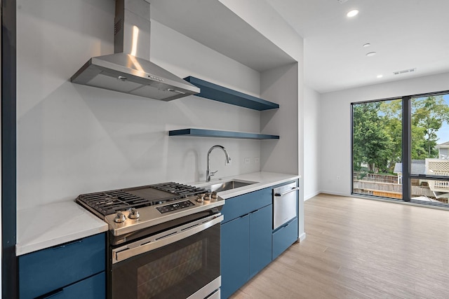 kitchen featuring blue cabinets, sink, wall chimney exhaust hood, light hardwood / wood-style floors, and stainless steel range with gas stovetop