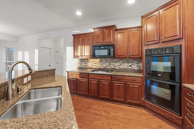 kitchen with light stone countertops, tasteful backsplash, sink, black appliances, and light hardwood / wood-style floors