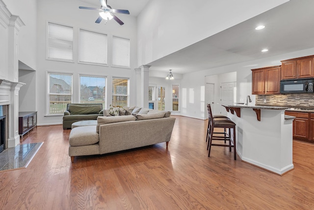 living room featuring ceiling fan with notable chandelier, light wood-type flooring, a high end fireplace, and a towering ceiling