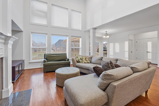 living room featuring a notable chandelier, wood-type flooring, a high ceiling, and decorative columns