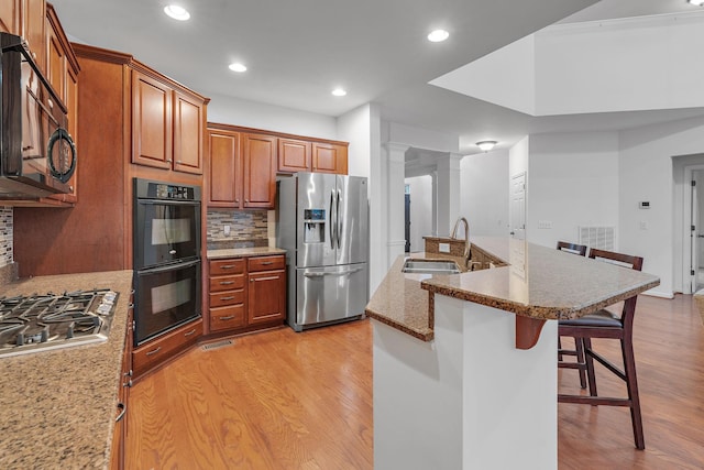 kitchen featuring a kitchen breakfast bar, tasteful backsplash, sink, black appliances, and light hardwood / wood-style flooring