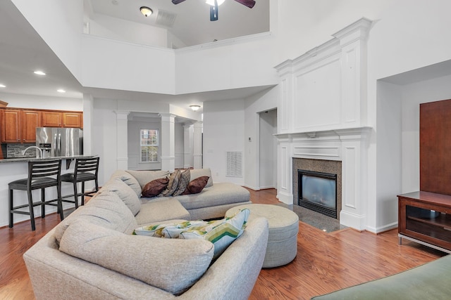 living room featuring a high end fireplace, ceiling fan, a high ceiling, and light hardwood / wood-style flooring