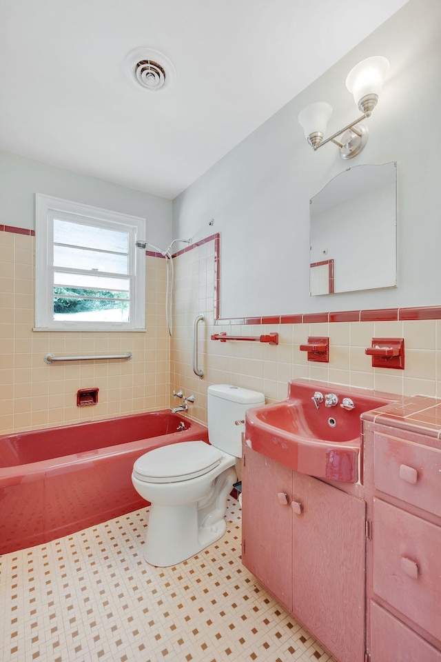 full bathroom with vanity, tile patterned floors, tiled shower / bath combo, toilet, and tile walls