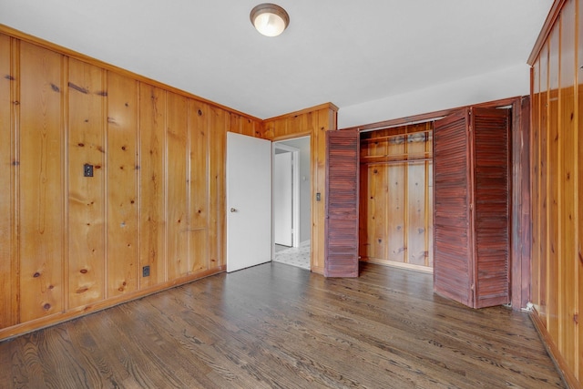 unfurnished bedroom featuring dark hardwood / wood-style floors, a closet, and wood walls