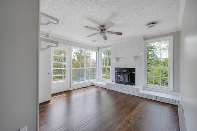 unfurnished living room with a wood stove, ceiling fan, dark wood-type flooring, crown molding, and a textured ceiling