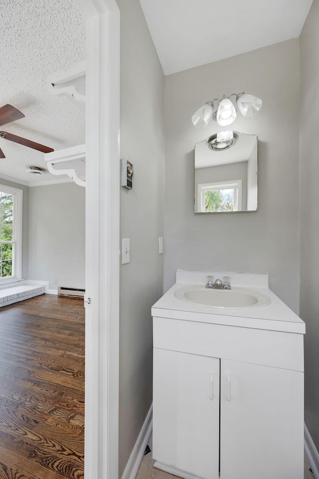 bathroom with hardwood / wood-style floors, vanity, ceiling fan, a textured ceiling, and baseboard heating