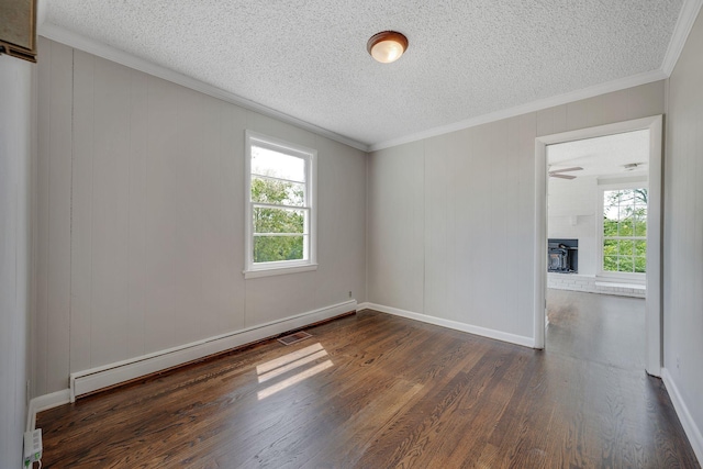 empty room featuring dark wood-type flooring, a wood stove, a wealth of natural light, and a baseboard heating unit