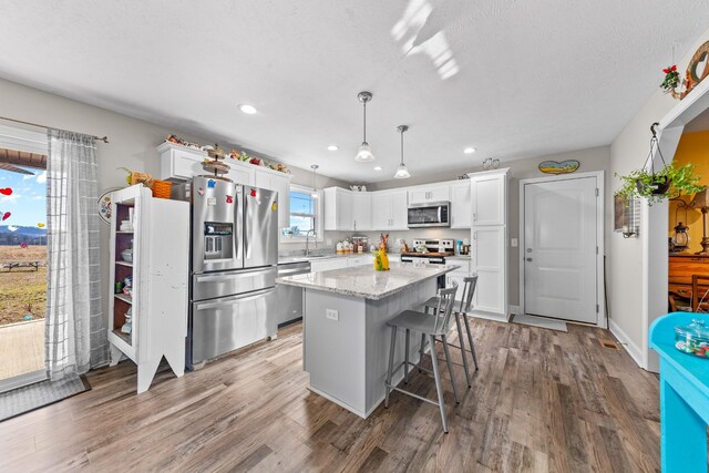 kitchen with stainless steel appliances, white cabinetry, a center island, and decorative light fixtures