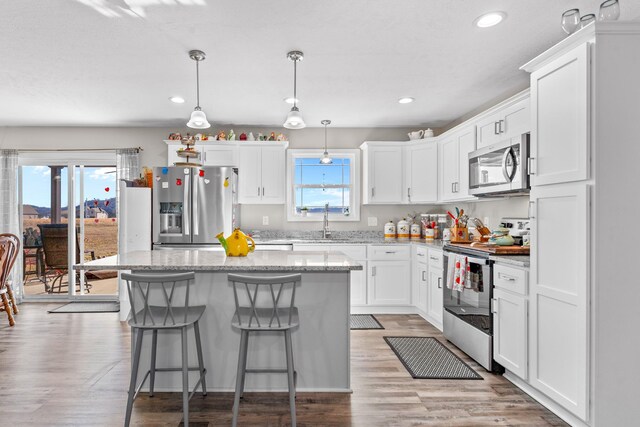 kitchen with sink, stainless steel appliances, white cabinets, a kitchen island, and decorative light fixtures