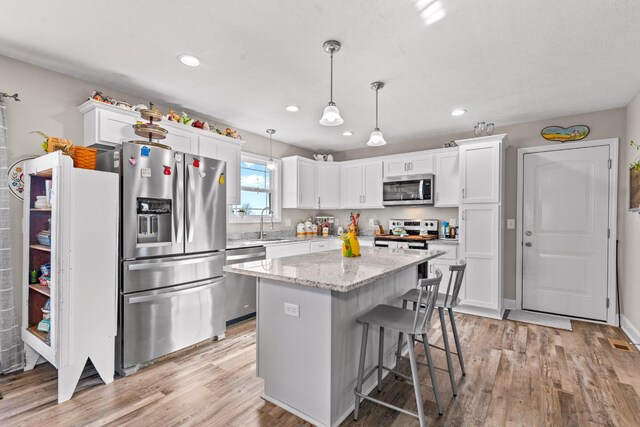 kitchen with a kitchen island, decorative light fixtures, white cabinetry, stainless steel appliances, and light stone countertops