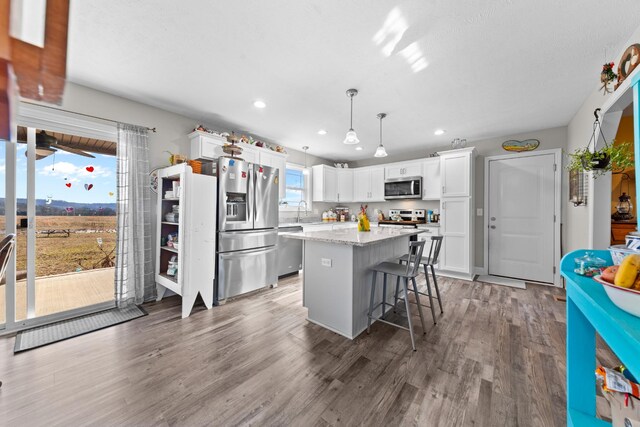 kitchen with a kitchen bar, white cabinetry, decorative light fixtures, a center island, and appliances with stainless steel finishes