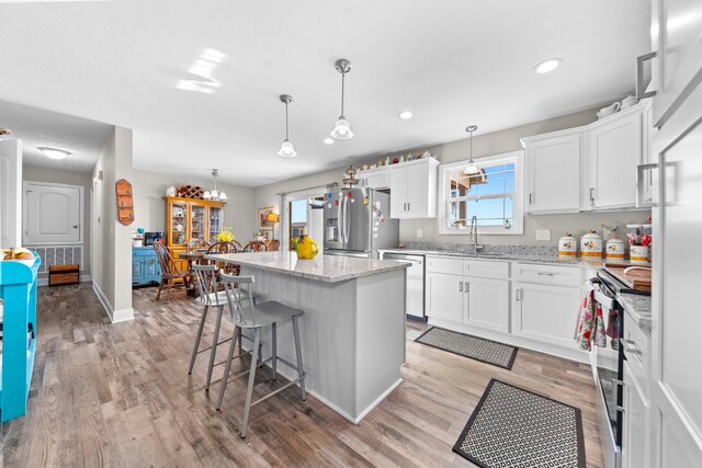 kitchen with white cabinetry, appliances with stainless steel finishes, a center island, and decorative light fixtures