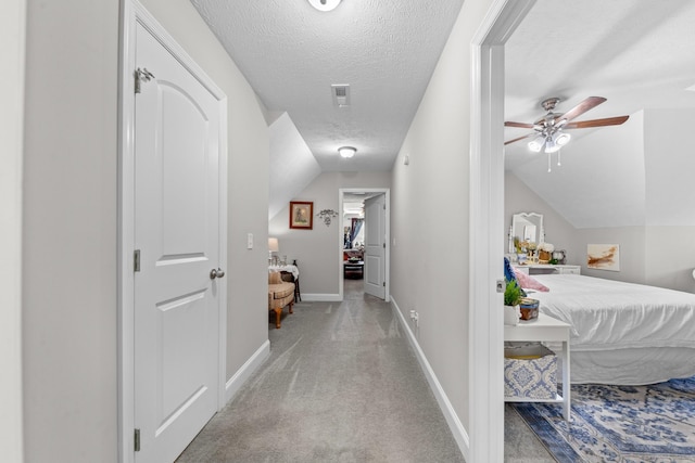 hall with vaulted ceiling, light carpet, and a textured ceiling