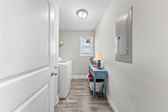 laundry room with a textured ceiling, electric panel, light hardwood / wood-style floors, and washing machine and clothes dryer