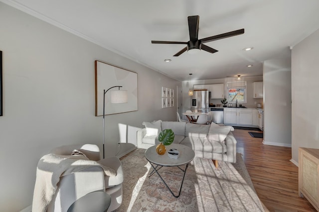 living room featuring ceiling fan, sink, light hardwood / wood-style flooring, and ornamental molding