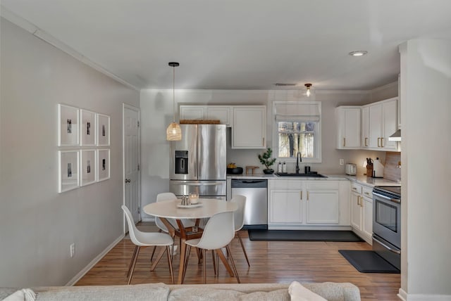 kitchen with white cabinetry, appliances with stainless steel finishes, decorative light fixtures, dark wood-type flooring, and sink