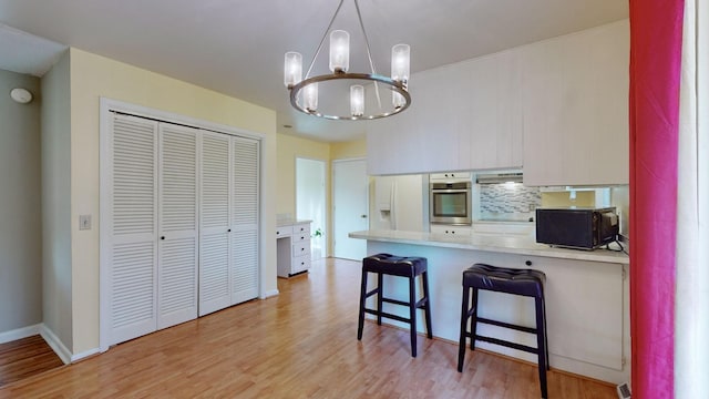 kitchen with stainless steel oven, white fridge with ice dispenser, a notable chandelier, kitchen peninsula, and a breakfast bar area