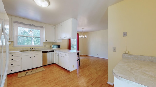 kitchen with sink, kitchen peninsula, pendant lighting, white cabinets, and appliances with stainless steel finishes